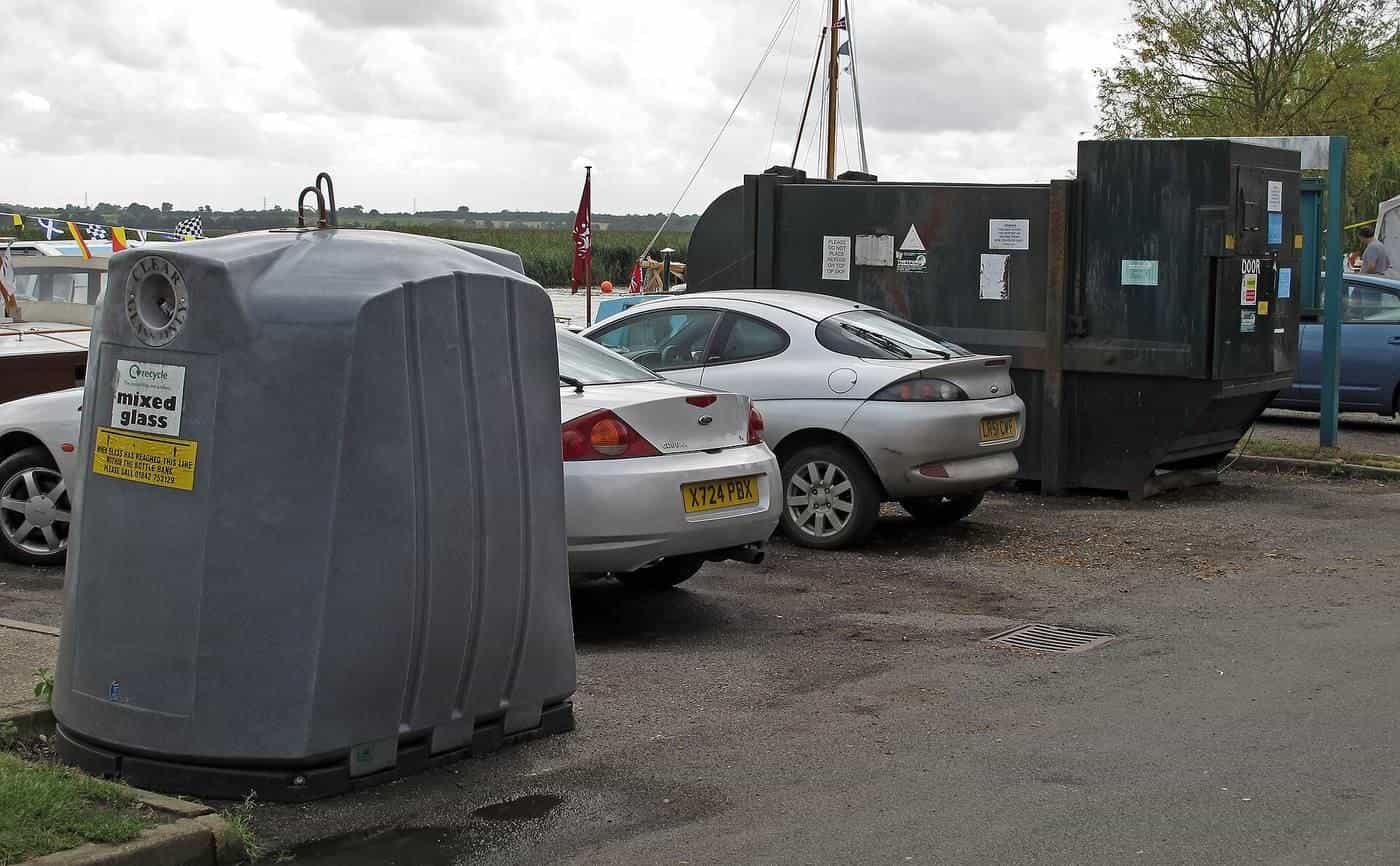 A rubbish skip and recycling bin in a car park beside parked cars