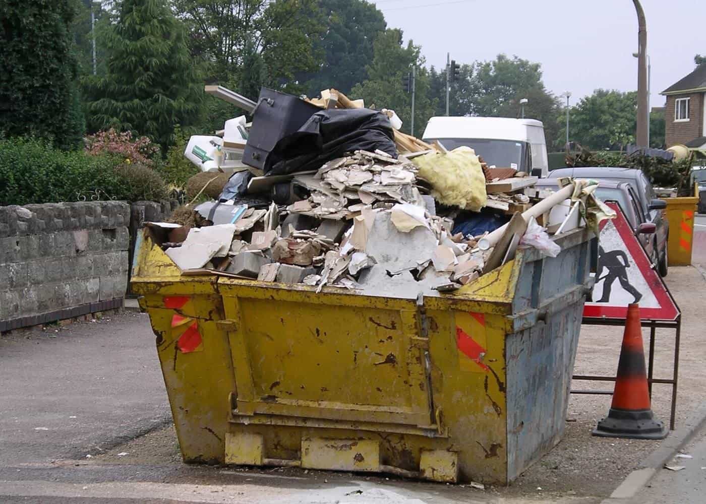A yellow skip filled with renovation rubble, plasterboard and timber beside a road