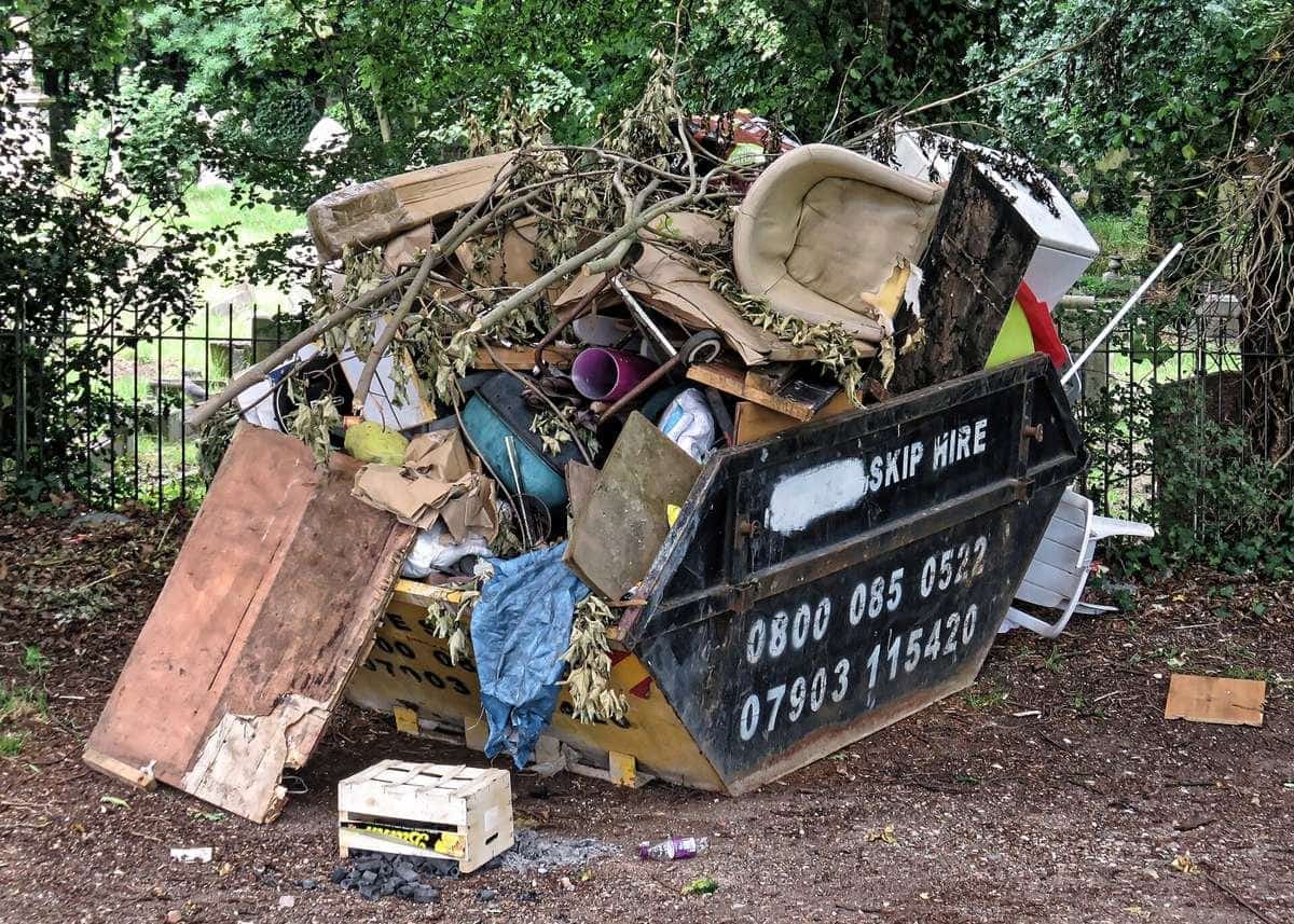 An overflowing skip with old furniture, timber and household junk piled above its sides
