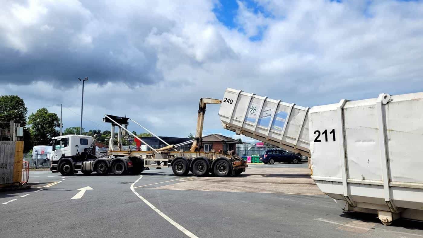 A skip truck lifting a large waste container on a wide road