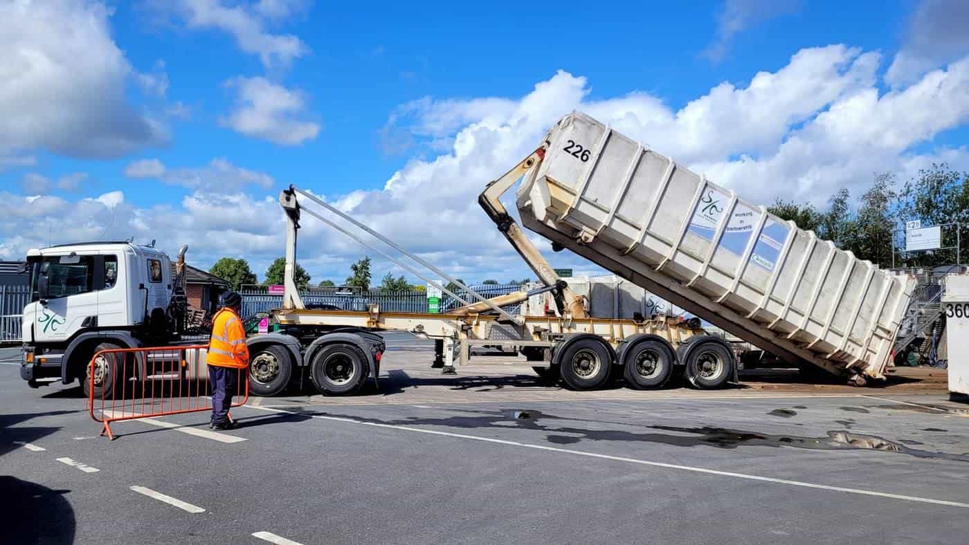 A hook-lift truck tipping a large roll-on roll-off waste container