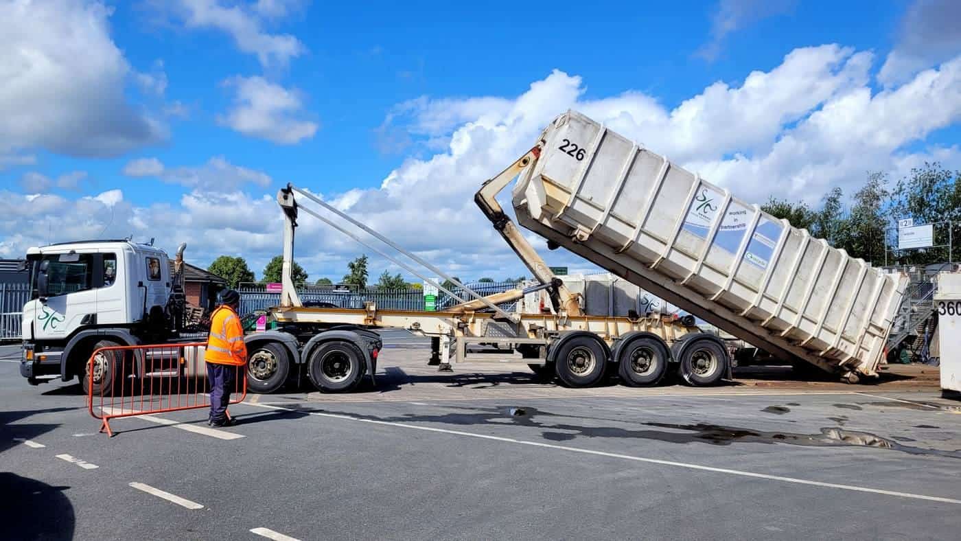 A hook-lift truck tipping a large roll-on roll-off waste container