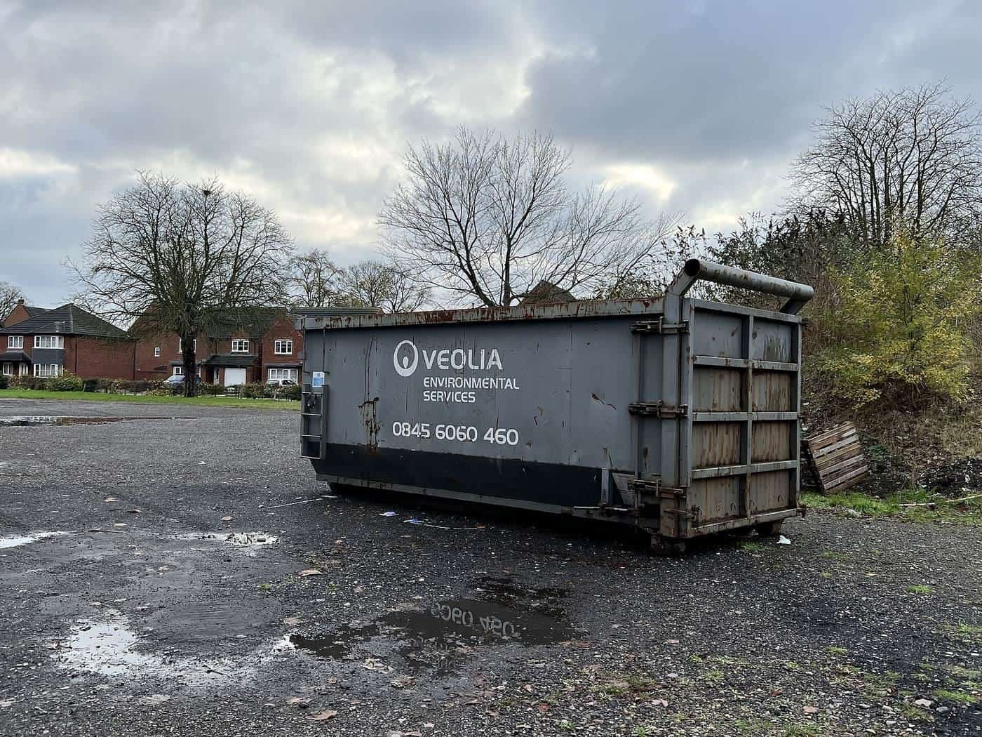 A large roll-on roll-off waste container on a wet gravel site