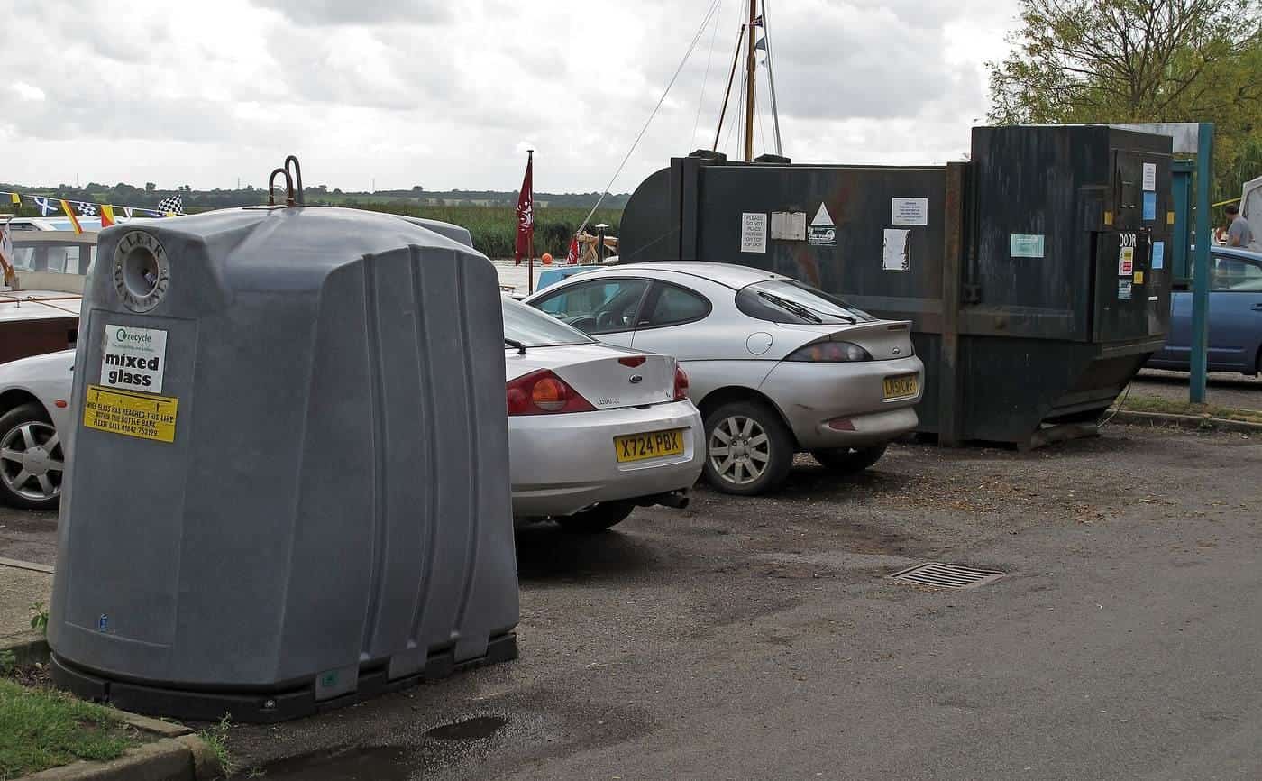 A rubbish skip and recycling bin in a car park beside parked cars